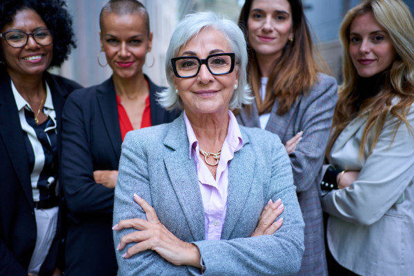 A group of five joyful mature business women of diverse races looking smiling at camera with arms crossed outdoor